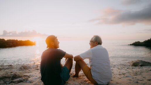 Zwei Männer sitzen bei Sonnenuntergang am Strand