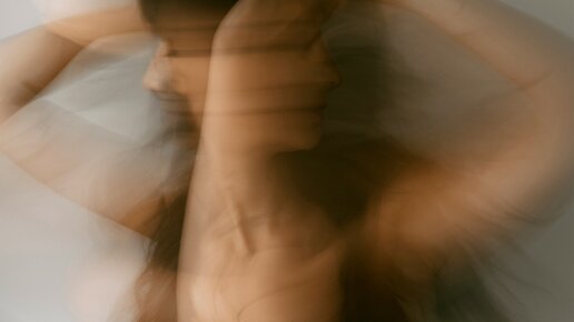 Unscharfe Bewegungsaufnahme einer Frau mit erhobenen Armen, künstlerischer Effekt mit warmen Farbtönen.