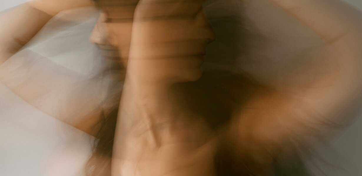 Unscharfe Bewegungsaufnahme einer Frau mit erhobenen Armen, künstlerischer Effekt mit warmen Farbtönen.