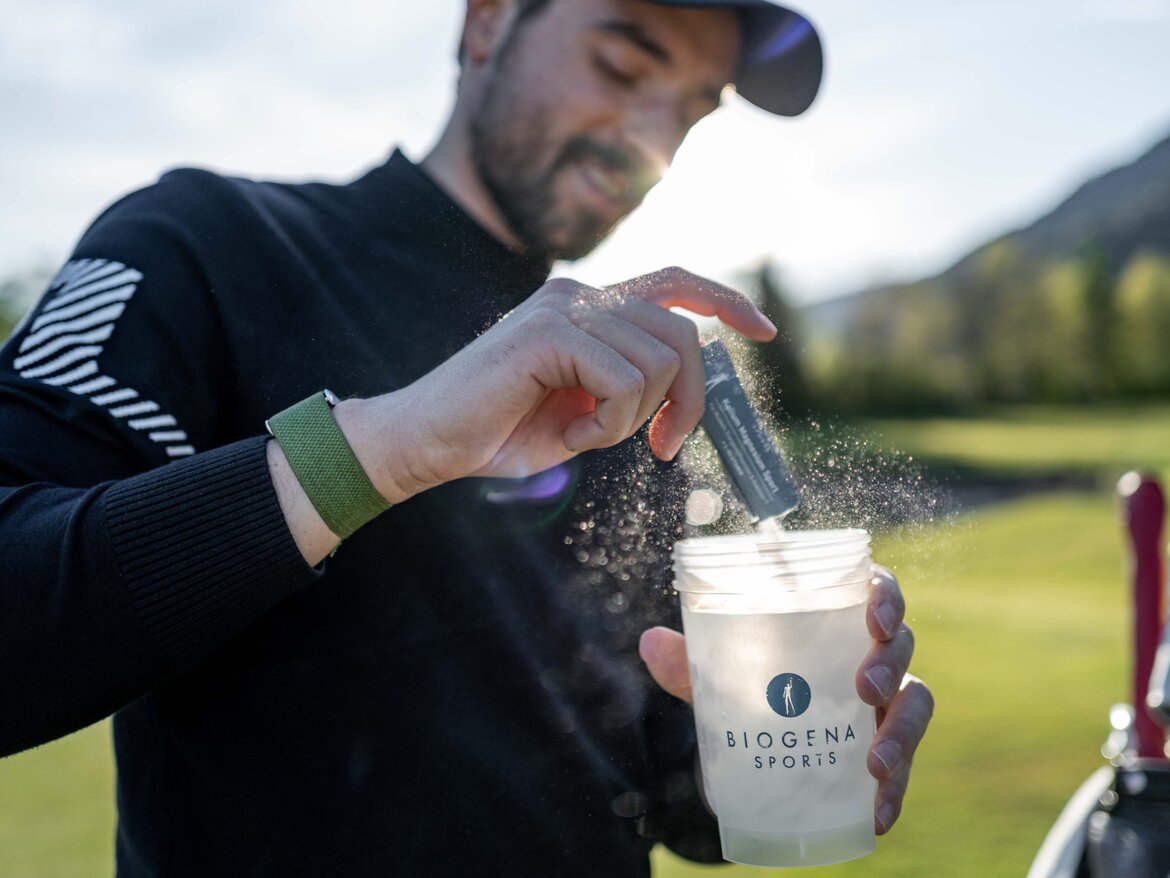 Golfista leje obsah BIOGENA SPORTS draslík horčík sáčku do BIOGENA SPORTS shakeru, zelená lúka v pozadí