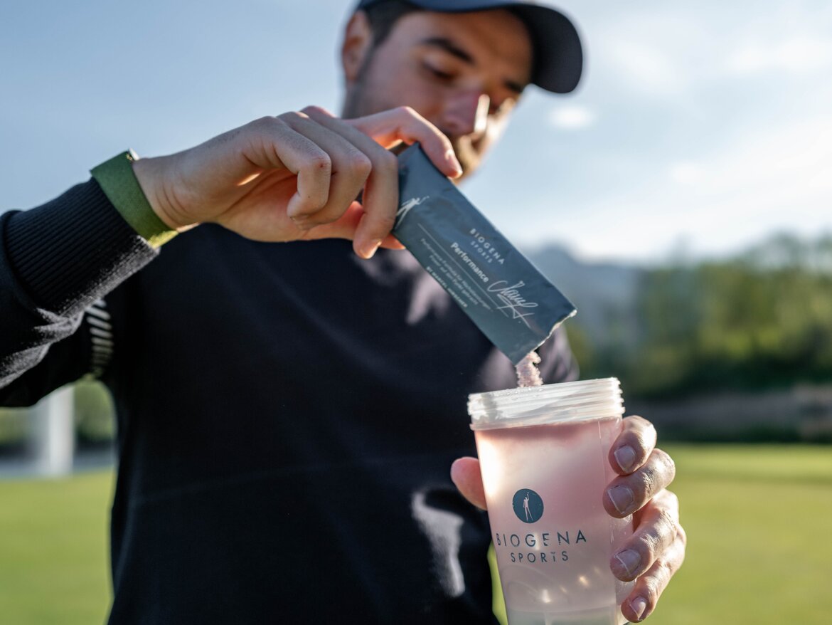 Un golfista vierte el contenido de un sobre de SPORTS Performance en el BIOGENA SPORTS Shaker, con un prado verde de fondo