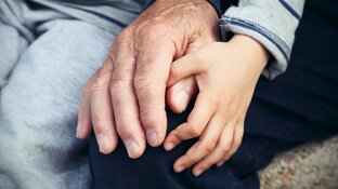 Eine ältere und eine kindliche Hand liegen sanft übereinander und symbolisieren generationsübergreifende Verbindung und Fürsorge.